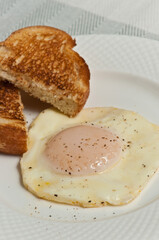 Top view, close distance of a fried egg with pepper, and two slices of toast, on a white, round plate