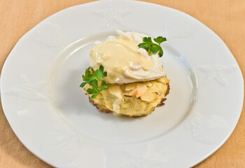 top view close up of an almond crusted crab cake with a poached egg and sprig of parsley on a white bowl 