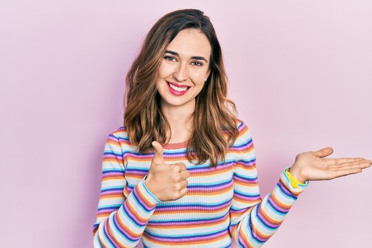 Young hispanic girl wearing casual clothes showing palm hand and doing ok gesture with thumbs up, smiling happy and cheerful
