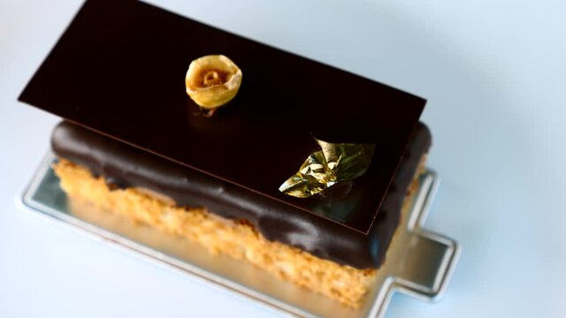 Close Up of Opera Cake Dessert with Hazelnut on White Plate in Restaurant. Tasty Cocoa Chocolate Piece of Cake with Edible Gold and Nut in Cafe. 4k