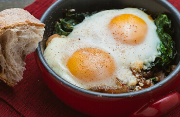 Baked eggs and spinach in a small baking dish on a red napkin.