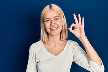 Beautiful blonde woman wearing casual sweater smiling positive doing ok sign with hand and fingers. successful expression.