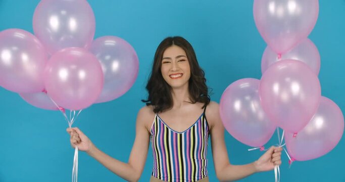 Portrait of young beautiful asian woman holding balloon in hand  with attractive smile in blue background. Pretty girl dance and look to camera with happy emotion. Fashion, travel and beauty concept.