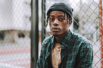 Handsome and stylish Spanish man posing with a chain-link fence on the background
