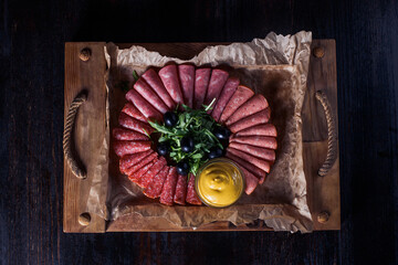 sausage cut with herbs and sauce on a wooden tray, beautiful serving, dark background