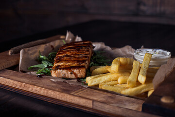 salmon fillet steak with french fries on a wooden tray, beautiful serving, dark background