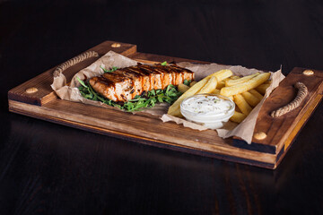 salmon fillet steak with french fries on a wooden tray, beautiful serving, dark background