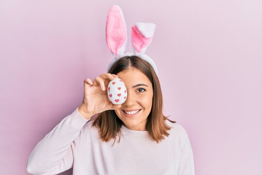 Young beautiful woman wearing cute easter bunny ears holding egg looking positive and happy standing and smiling with a confident smile showing teeth