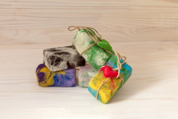 Natural handmade soap in colored wool with red heart on light natural wooden background. The concept of a washcloth peeling. Self-care, commitment to eco-friendly products.