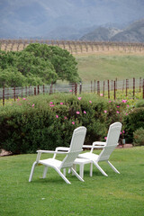 Two white chairs in a garden overlooking a vineyard landscape