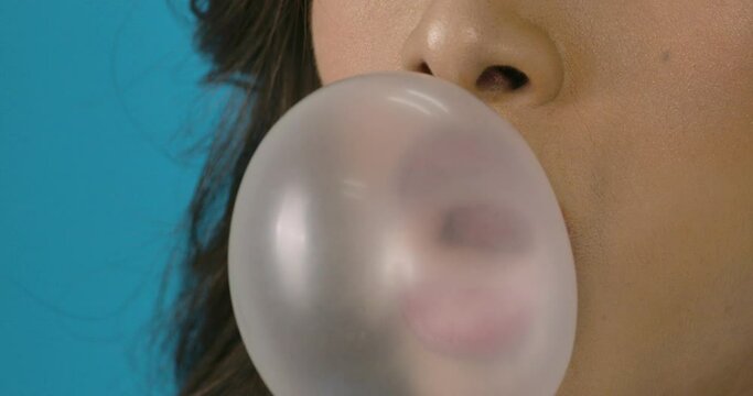 Portrait and big close up shot of young beautiful asian woman blowing gum in blue background. Fashion, travel and beauty concept.