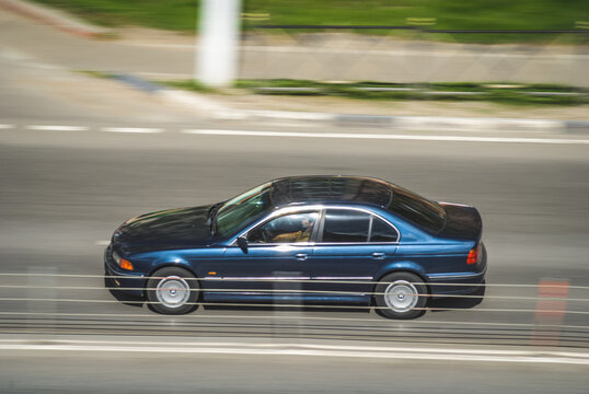 Old blue BMW E39 5 series on the city road. Fast moving car on the street. Vehicle driving along the street in city with blurred background. Accelerating with low-emission.