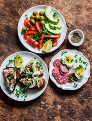 Snack, appetizers, tapas, breakfast table - salami, mackerel cream cheese sandwiches, olives, avocado, tomatoes, micro greens on a wooden background, top view