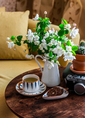 Cozy apartment still life - a cup of green tea, cookies, a bouquet of flowers, a camera on a wooden table next to the sofa