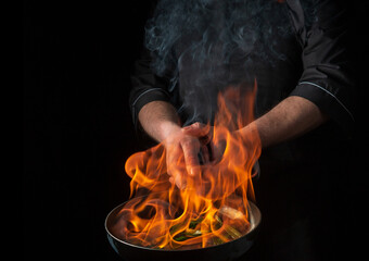 Chef or cook cooking food in pan with fire flame on black background. Restaurant and hotel service...