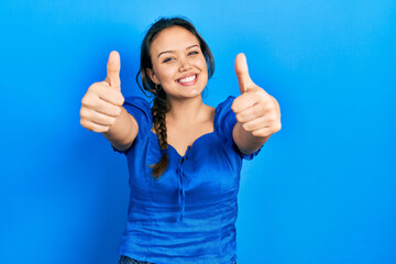 Young hispanic girl wearing casual clothes approving doing positive gesture with hand, thumbs up smiling and happy for success. winner gesture.