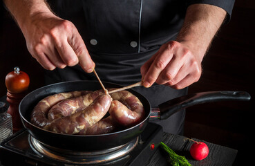 Close-up hands of chef or cook tying a thread of homemade sausage. Cooking sausages with meat and spices on a pan. Working environment in restaurant kitchen