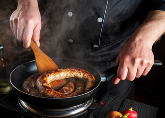 Cooking meat sausage in restaurant kitchen. Cook or chef fries sausage in a frying pan. The idea of a delicious meat dish