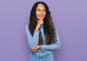 Young hispanic woman with curly hair wearing casual clothes with hand on chin thinking about question, pensive expression. smiling with thoughtful face. doubt concept.