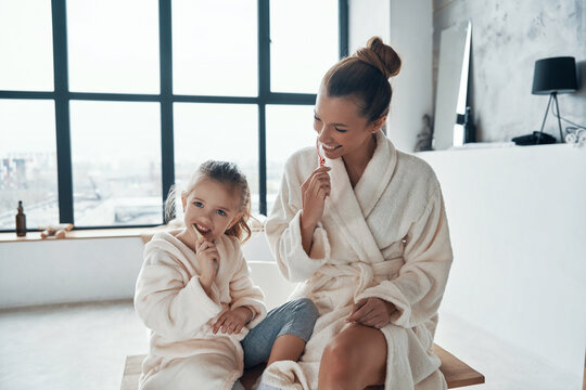 Mother and daughter in bathrobes smiling and cleaning teeth 