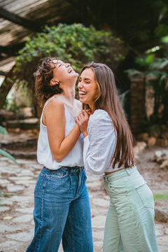 Two young teenager girl friends laughing surrounded by plants.