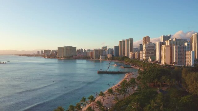 Panning aerial drone slowly flying over a colorful Honolulu Skyline while Sunset in Oahu, Hawaii with Waikiki Beach Shooting from a bird's eye view. Magnificent mountains of Hawaiian island of Oahu.