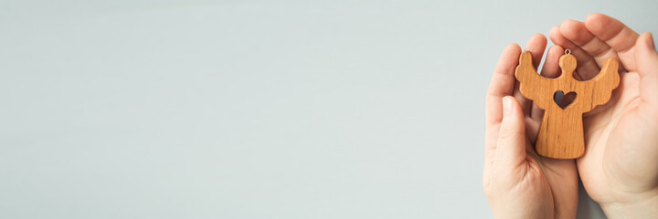 hands holding wooden angel figurine toy on blue background with copy space. concept of faith, hope, love, Christmas, charity, help and support, social responsibility.