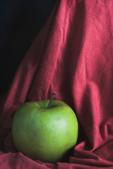 A green apple on a red cloth background . The concept of proper nutrition and a healthy lifestyle.