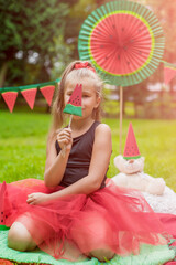 Watermelon party, picnic for children in park. watermelon day. Cute small girl with hat and with toy bear with watermelon hat