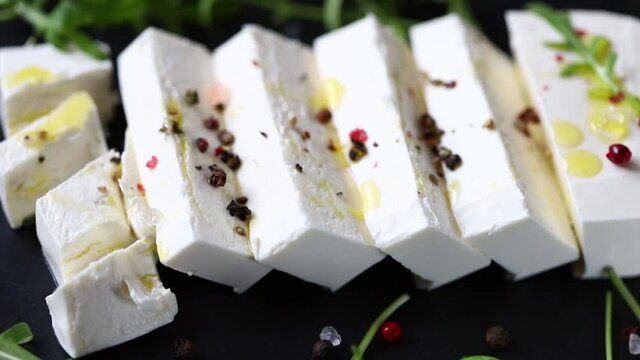Sliced feta cheese on a black stone board with spices and olive oil.