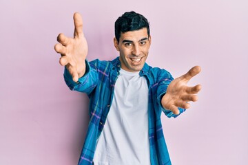 Handsome hispanic man wearing casual clothes looking at the camera smiling with open arms for hug. cheerful expression embracing happiness.