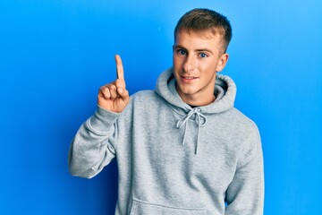 Naklejka premium Young caucasian man wearing casual sweatshirt smiling with an idea or question pointing finger up with happy face, number one