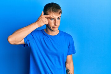 Naklejka premium Young caucasian man wearing casual blue t shirt pointing unhappy to pimple on forehead, ugly infection of blackhead. acne and skin problem
