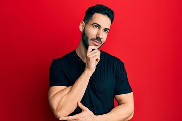 Young hispanic man wearing casual black t shirt thinking concentrated about doubt with finger on chin and looking up wondering