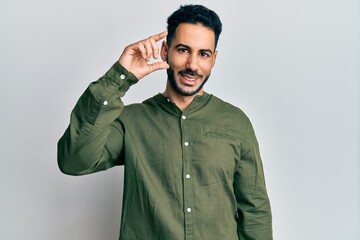 Young hispanic man wearing casual clothes smiling and confident gesturing with hand doing small size sign with fingers looking and the camera. measure concept.