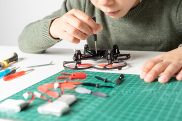 View of concentrated boy repairing his toy drone with a screwdriver in his hand and various spare parts for his drone. Selective focus