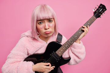 Horizontal shot of pink haired woman dressed in fur coat plays black acoustic guitar wants to...