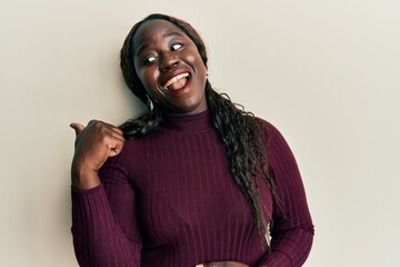 African young woman wearing casual clothes pointing thumb up to the side smiling happy with open mouth