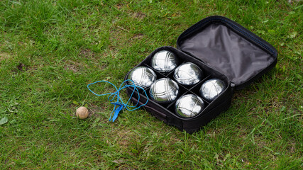 Naklejka premium Petanque set with six metal balls and a blue measuring rope in a black case on green grass. Play in your own garden during quarantine.
