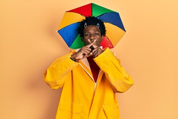Young african american man wearing yellow raincoat rejection expression crossing fingers doing negative sign