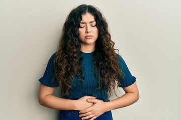 Young brunette woman with curly hair wearing casual clothes with hand on stomach because indigestion, painful illness feeling unwell. ache concept.