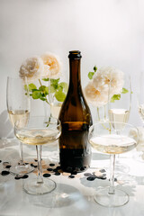 Blank bottle of champagne and full glasses with pale pink roses on background.