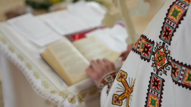 A priest in a cassock is reading the Bible. The priest prays while standing in the church. An Orthodox priest conducts a prayer ceremony.