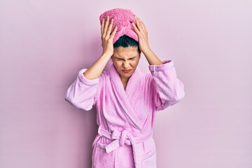 Young hispanic woman wearing shower towel cap and bathrobe suffering from headache desperate and stressed because pain and migraine. hands on head.