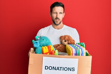 Young handsome man holding donation box with toys winking looking at the camera with sexy...