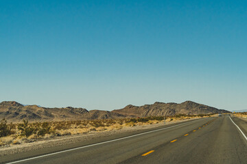 Two lane road in the arid Sierra Nevada's leading to mountains against blue sky