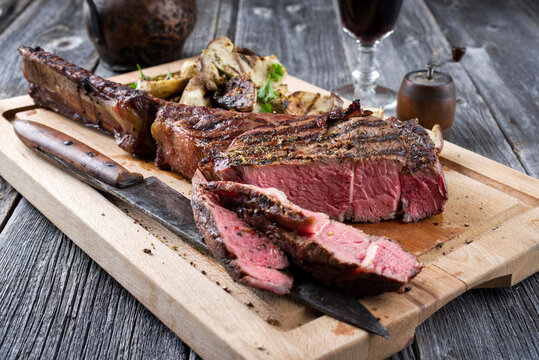 Traditional barbecue angus tomahawk beef steak with mushrooms served as close-up on a rustic wooden board