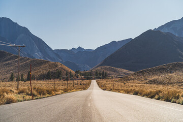 Two lane road in the arid Sierra Nevada's leading to mountains against blue sky