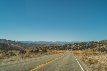 Two lane road in the arid Sierra Nevada's leading to mountains against blue sky