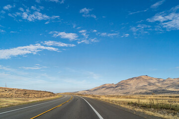 Fototapeta na wymiar Two lane road in the arid Sierra Nevada's leading to mountains against blue sky